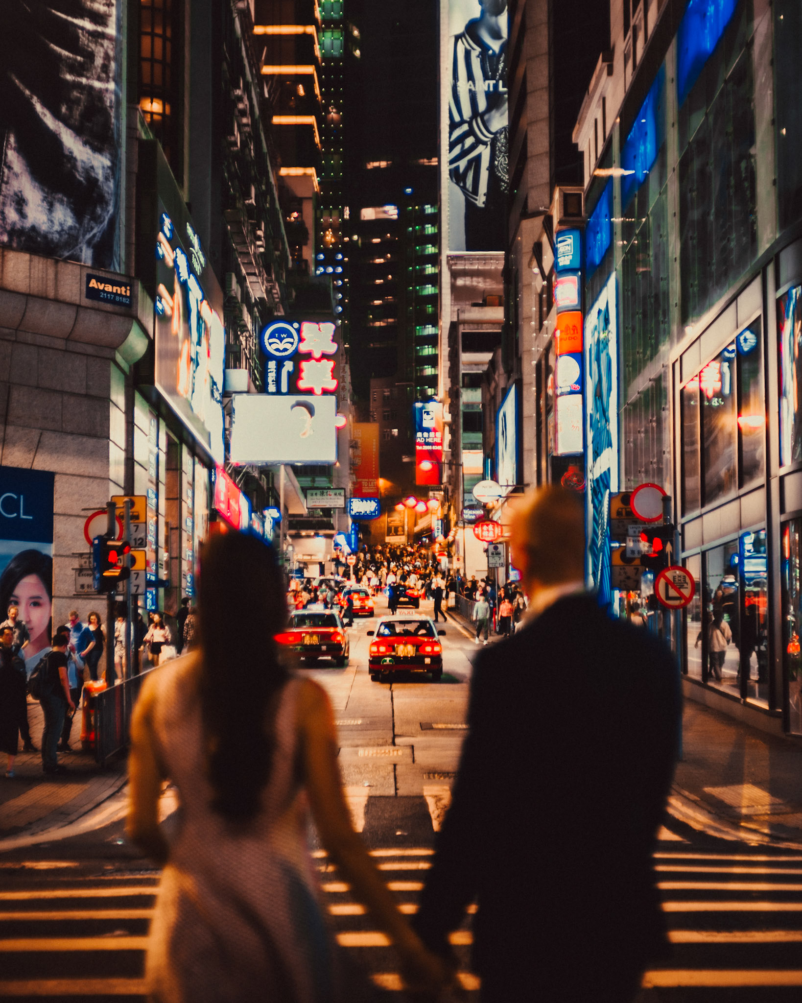 Night city couple portraits in bustling Queen's Road with an iconic taxi cab focused in the background, from Eric and Sabrina's engagement session in Central, Hong Kong, April 2019, Sony A7III.