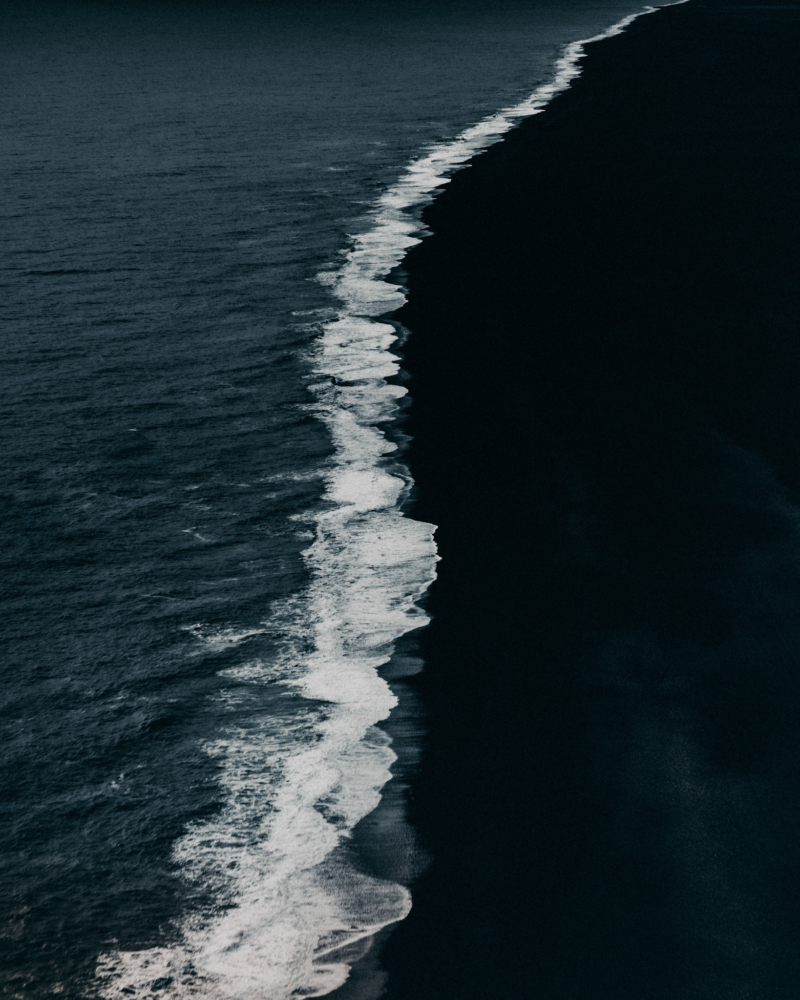 A long stretch of black sand with white crashing waves, as seen from Dyrhólaey Viewpoint, Iceland, May 2016, Sony A7RII.