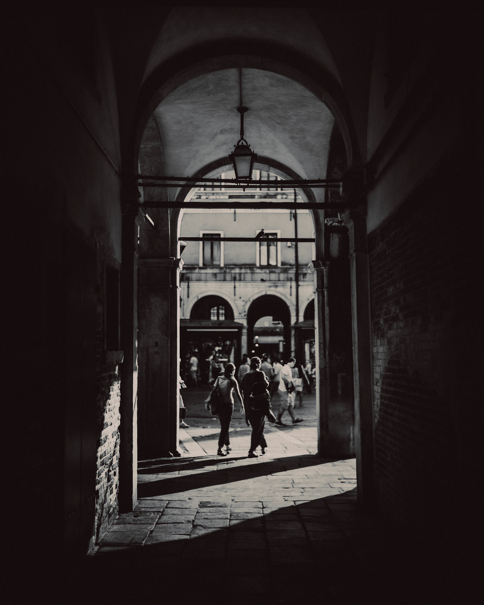 Two woman walking under an archway in Campo San Giacomo di Rialto, in black and white, Venice, Italy, August 2017, Leica M.