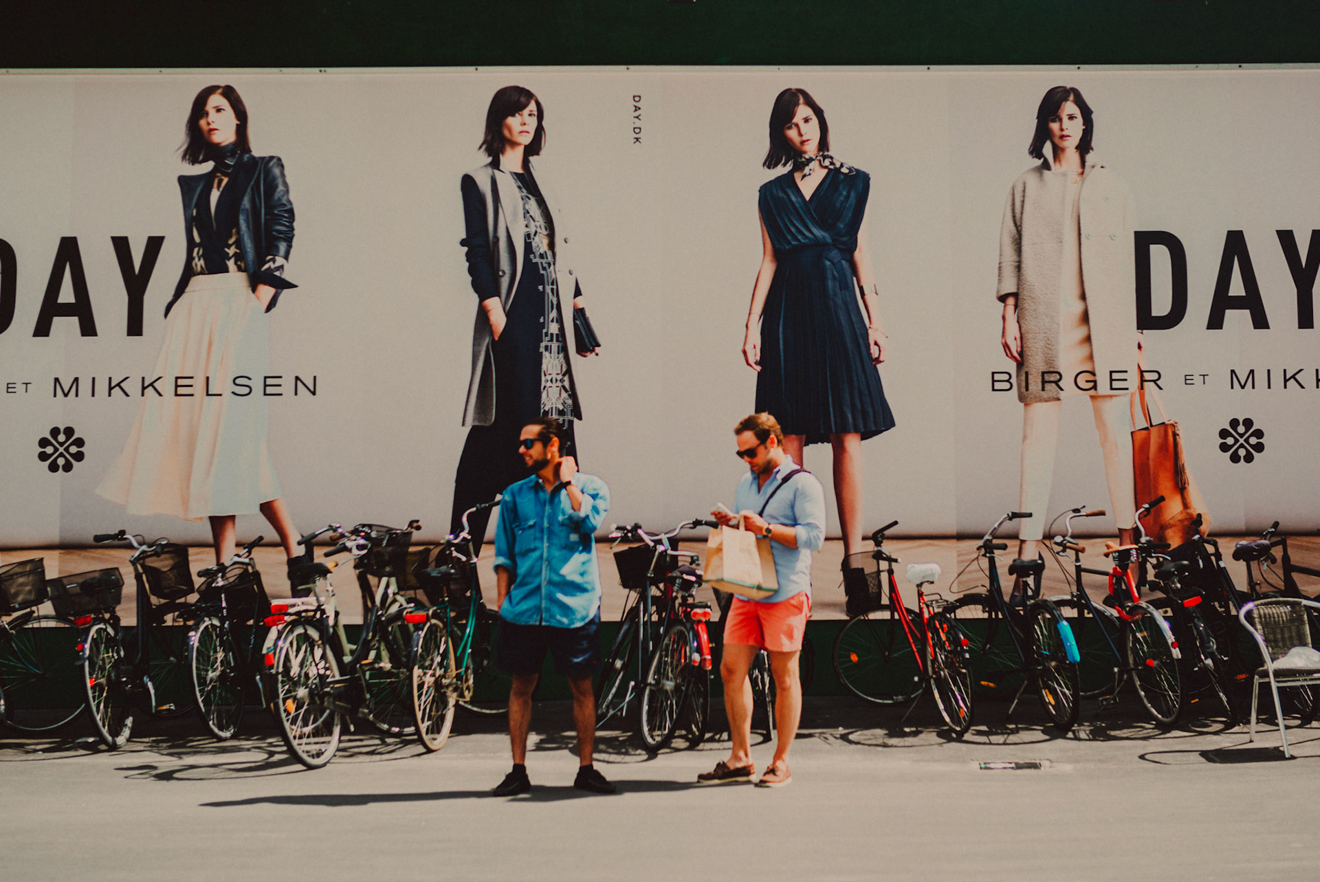 Two men in front of a billboard in Strøget, Copenhagen, Denmark, August 2015, Leica M.