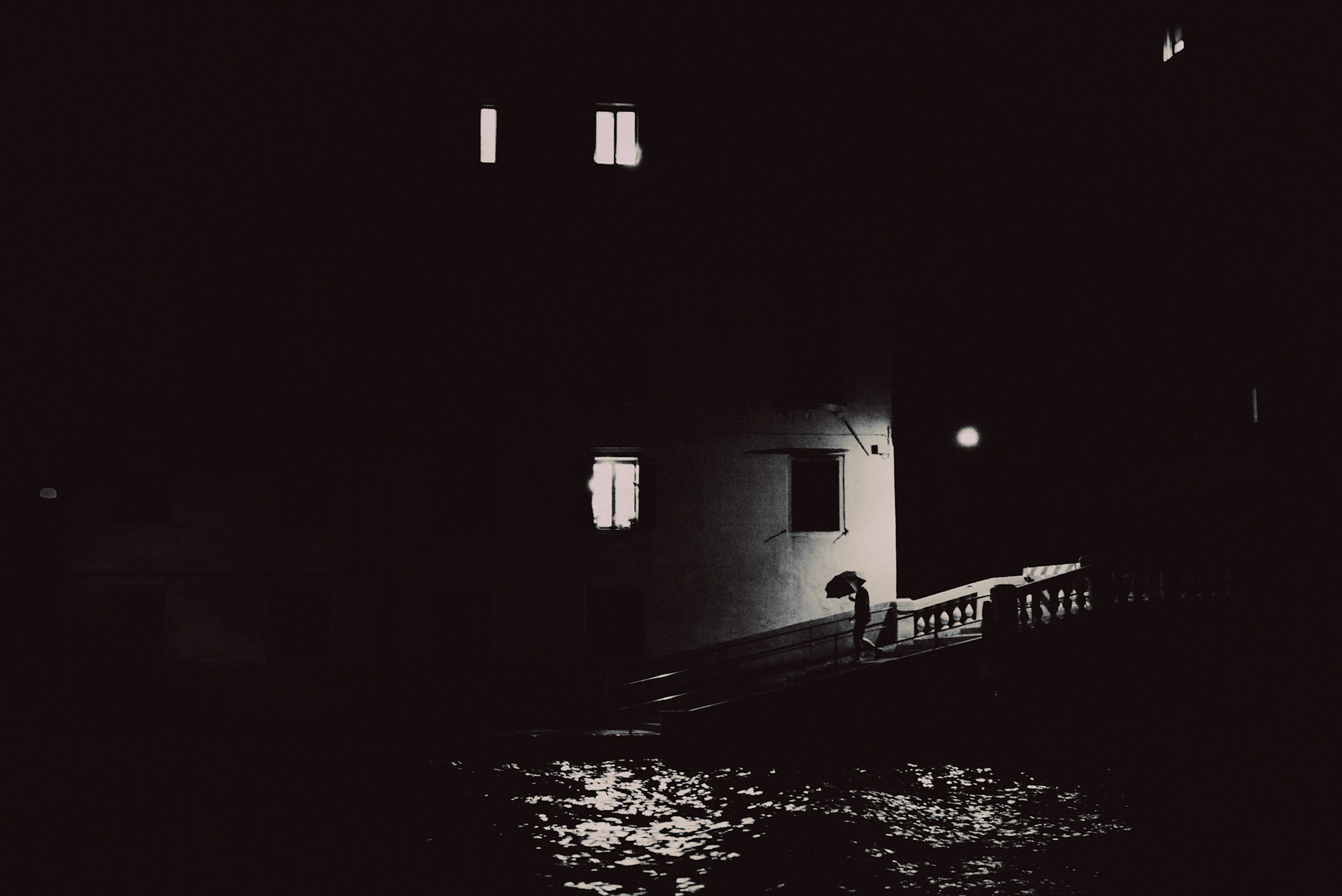 A man holdiong an umbrella in Murano at night, in black and white, Venice, Italy, July 2015, Leica M.