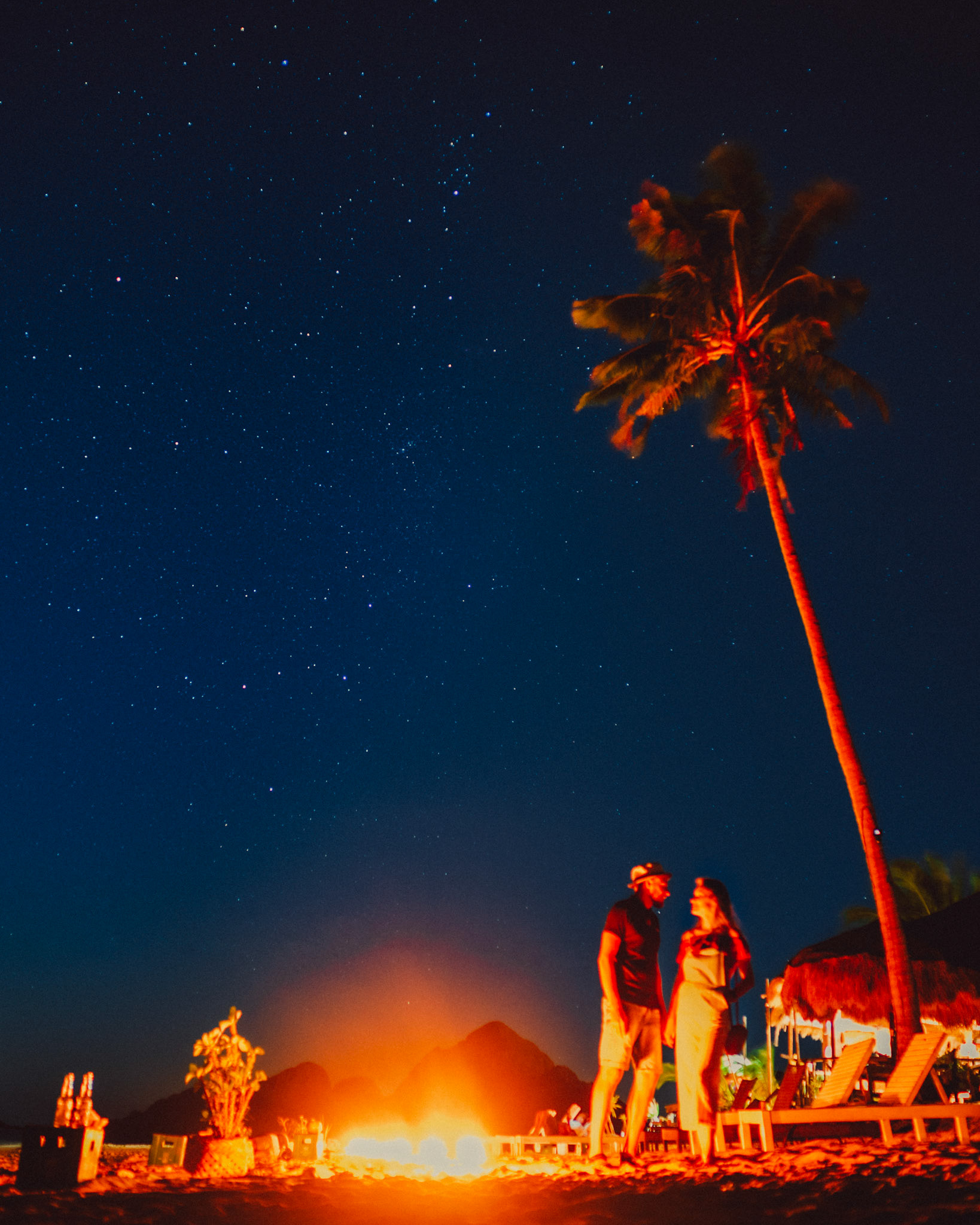 A starry night sky in Las Cabanas Beach with a couple beside a bonfire, El Nido, Palawan, Philippines, Southeast Asia, February 2019, Sony A7III.