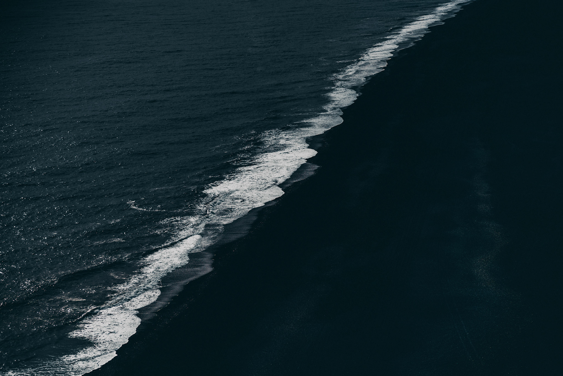 Black-to-black. A moody and minimalist landscape photo of dark waters and the pounding white surf crashing onto a black sand beach, Dyrhólaey, Iceland, May 2016, Sony A7RII.