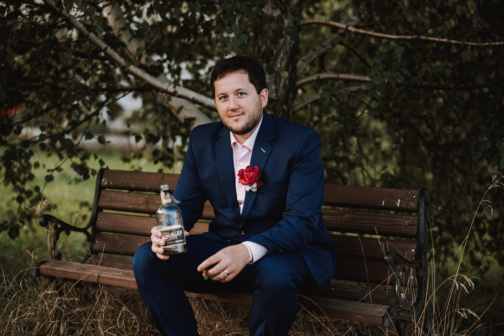 elegantní ženich pózuje na lavičce s lahví dobrého rumu