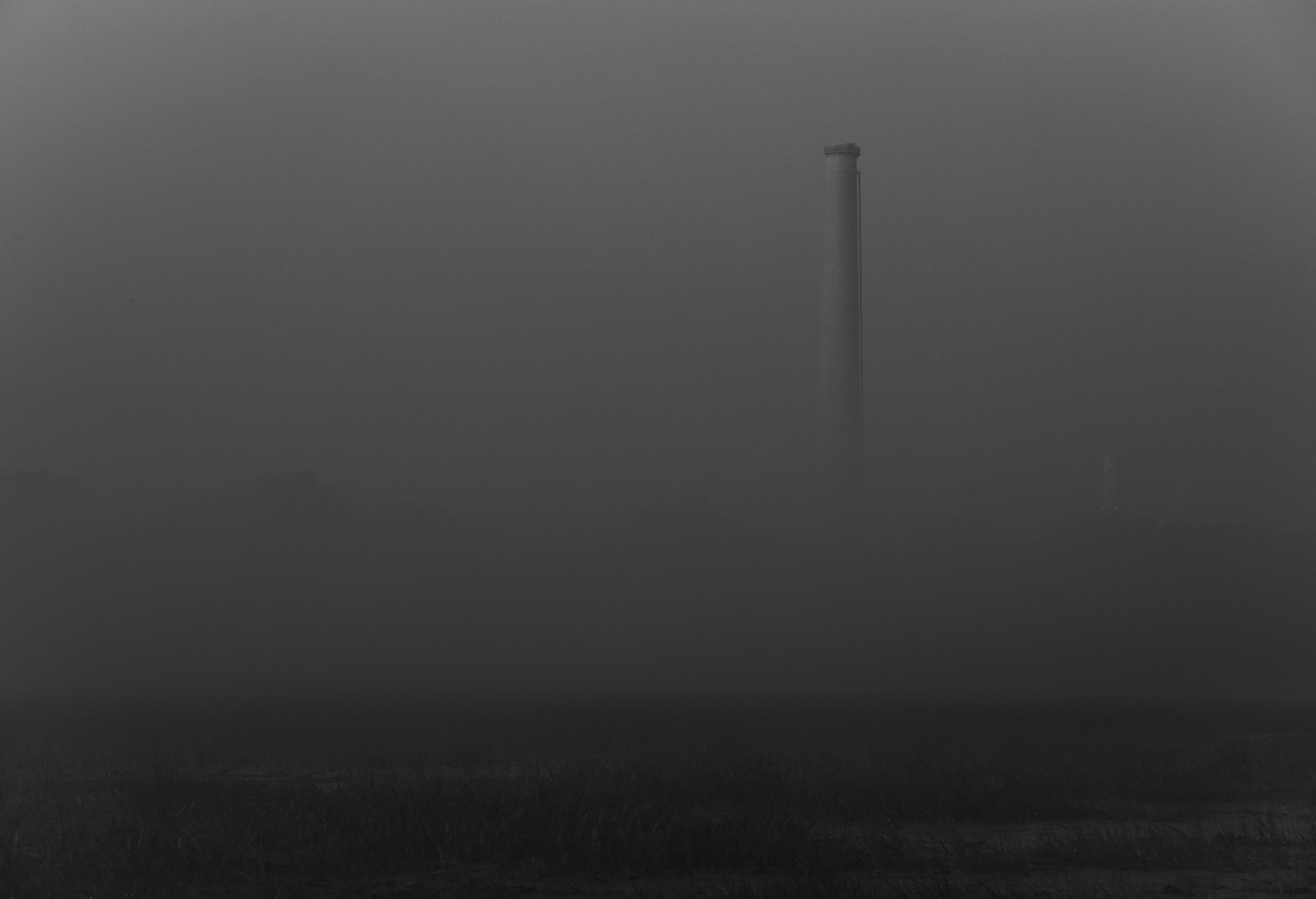 The smokestack emerges from the fog on a black-and-white morning.