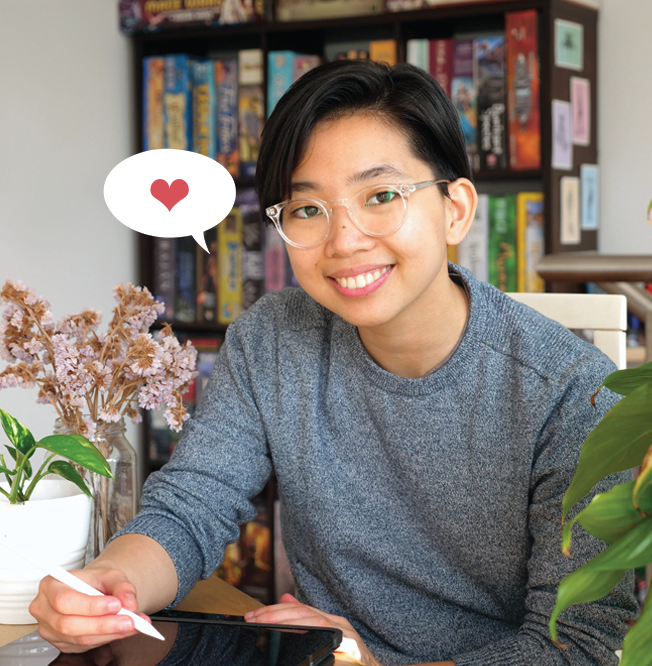A picture of Vee Hendro smiling with hand poised over drawing tablet and detailed with a small illustrative speech bubble with a "❤" in it.