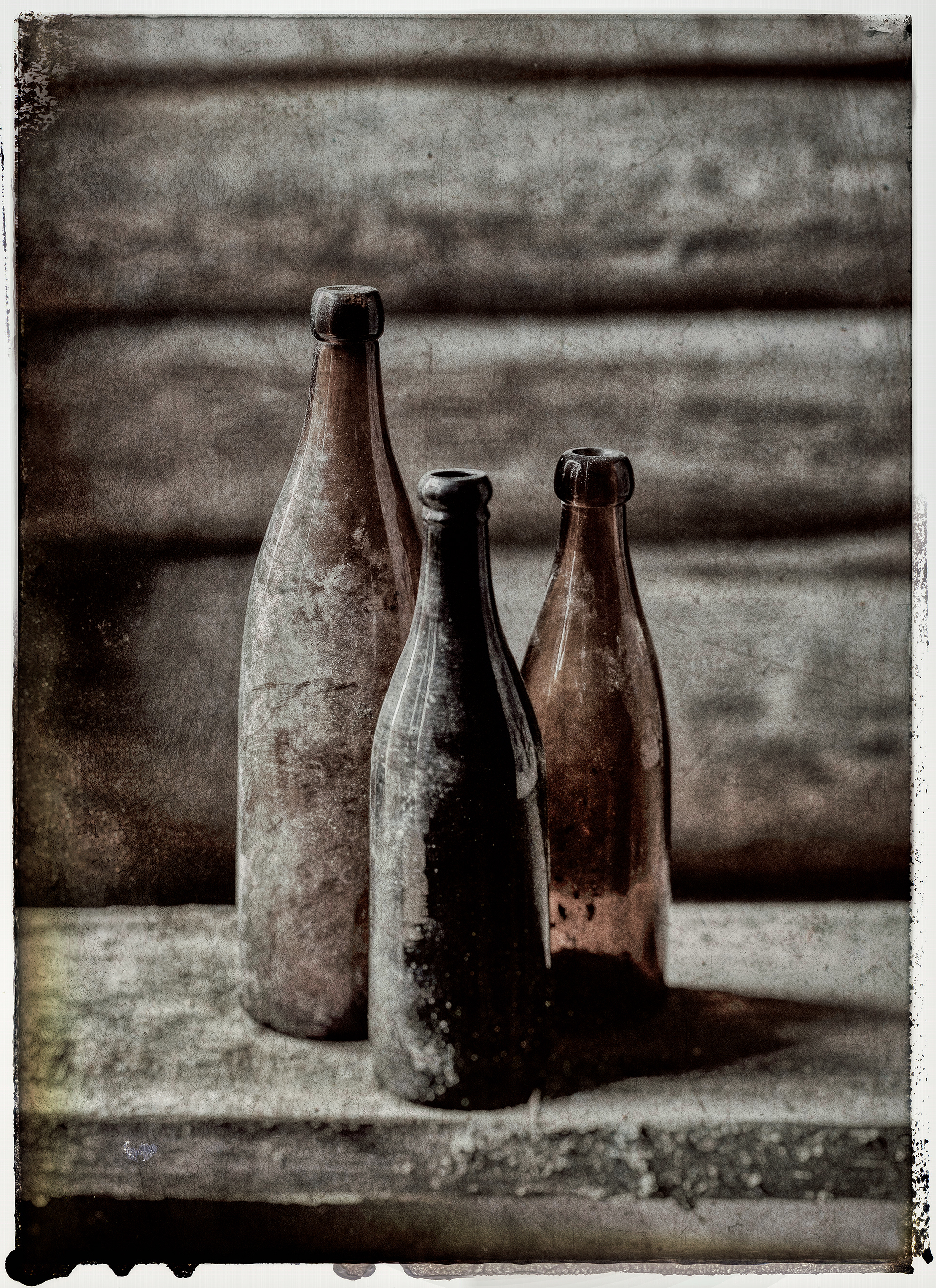 3 old dusty empty bottles on a plank against a timbered wall. Photographed with a dirty grimy look with a frayed border 