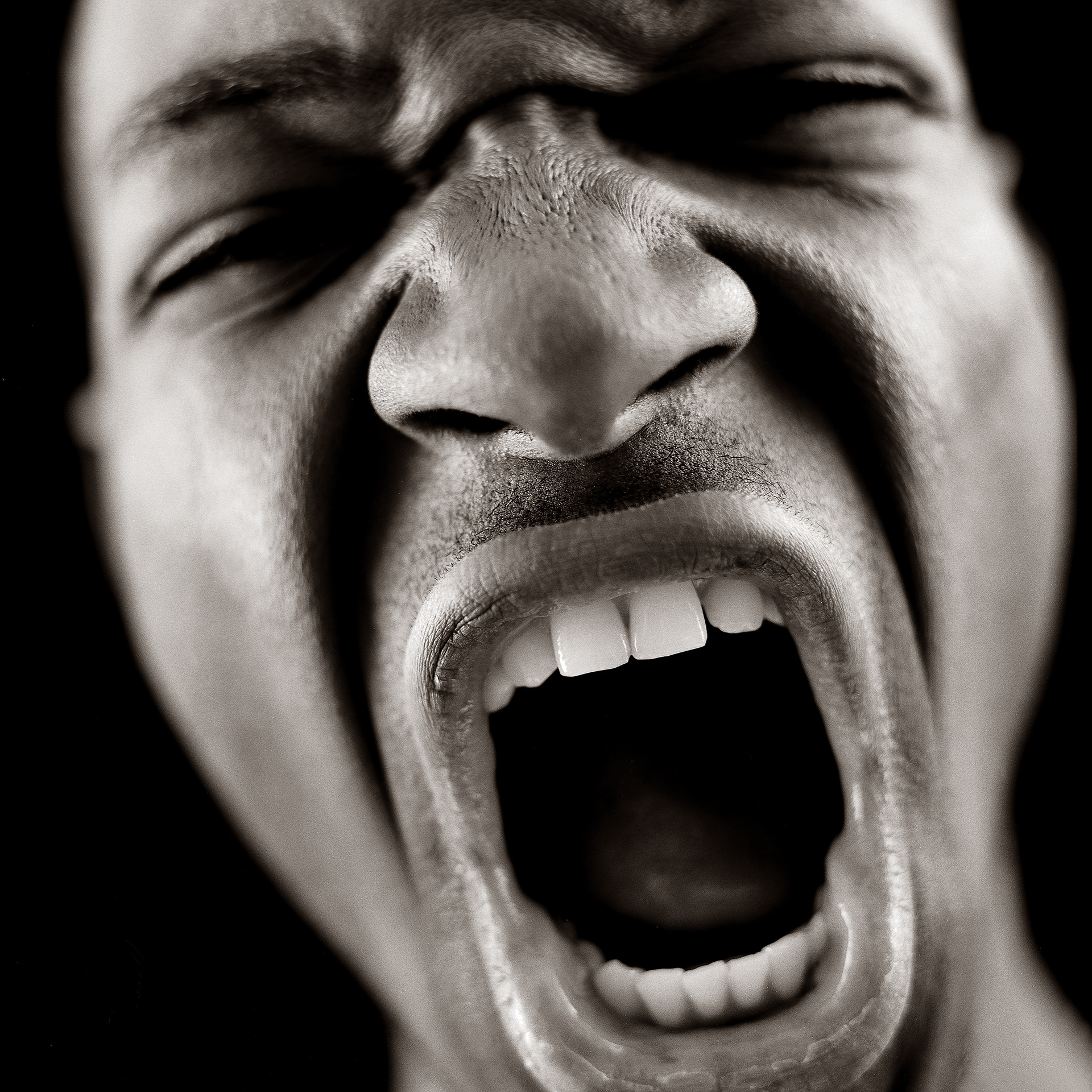 Close up of  dark skinned jovans face sceaming at the camera with short depth of field against a black background in black and white