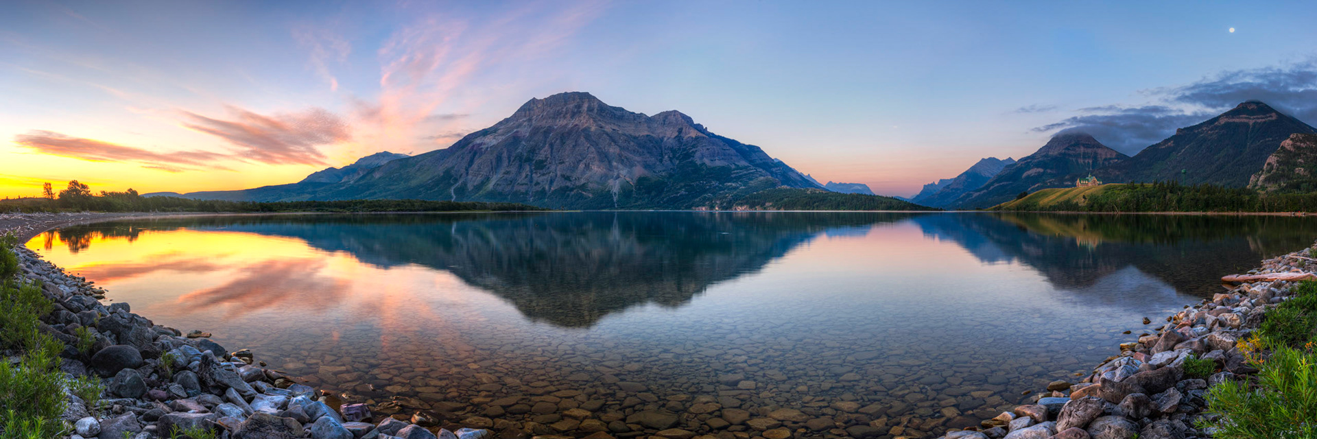 Panoramic sunrise from the north shore of Middle Waterton Lake.  Some peaks in Glacier National Park (Montana, US) can also be seen in the distance.Waterton Lakes National ParkAugust 2, 2015This is an HDR panoramic image consisting of 9 frames comprised of 5 exposures each. HDR processing performed in Photomatix Pro.  Panoramic stitching performed in Photoshop. Additional processing performed in Lightroom and Photoshop.PENTAX K-3, Sigma 10-20mm f/4-5.6 EX DCISO 100 19 mm  0.5 sec at ƒ / 11
