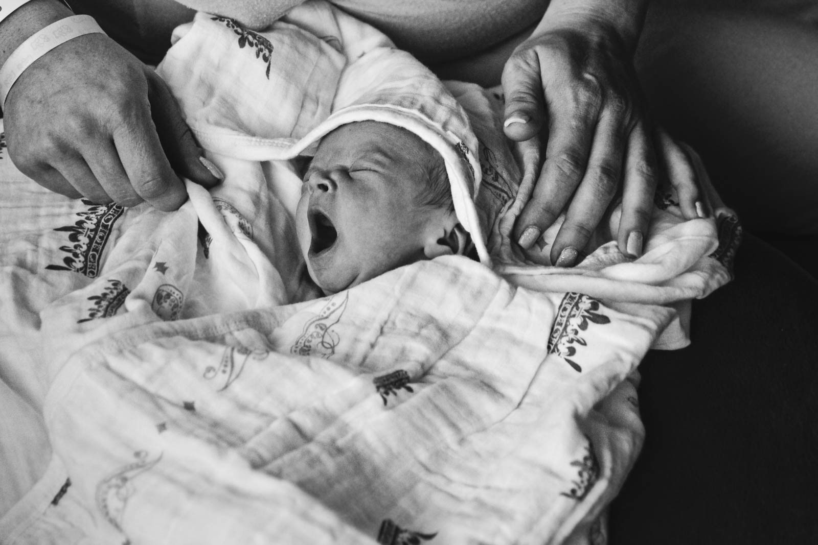 Newborn baby wrapped up in blanket in mother's lap yawns