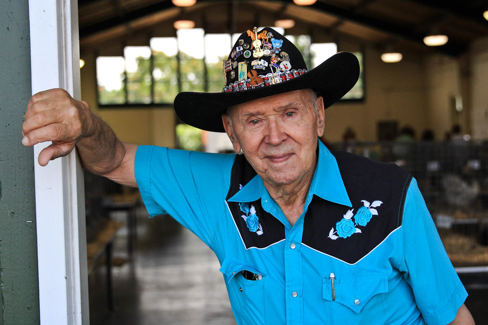 Portrait of elderly man in blue dress shirt and cowboy hat casually leans in doorway