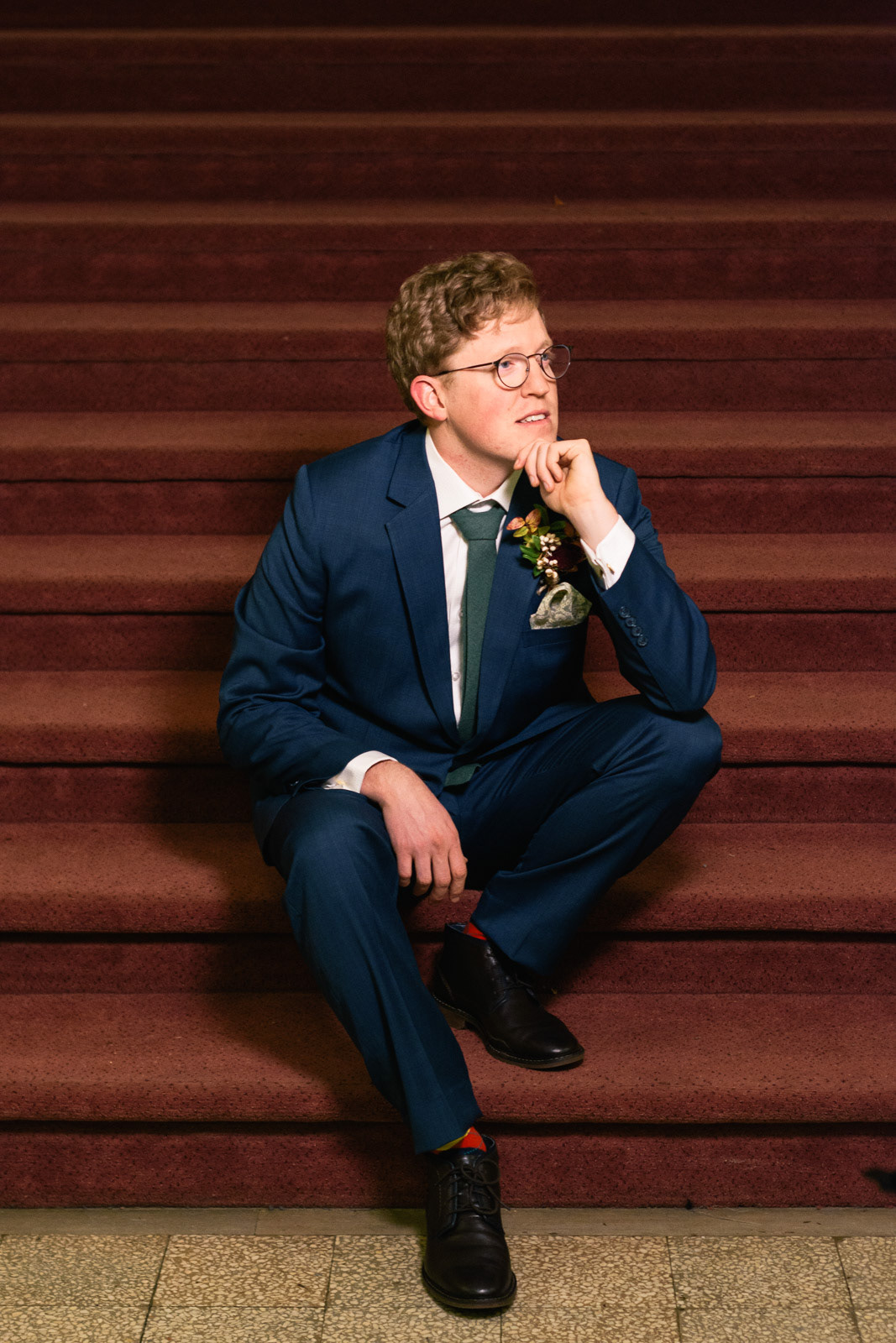 Groom in blue suit on a grand maroon-carpeted staircase