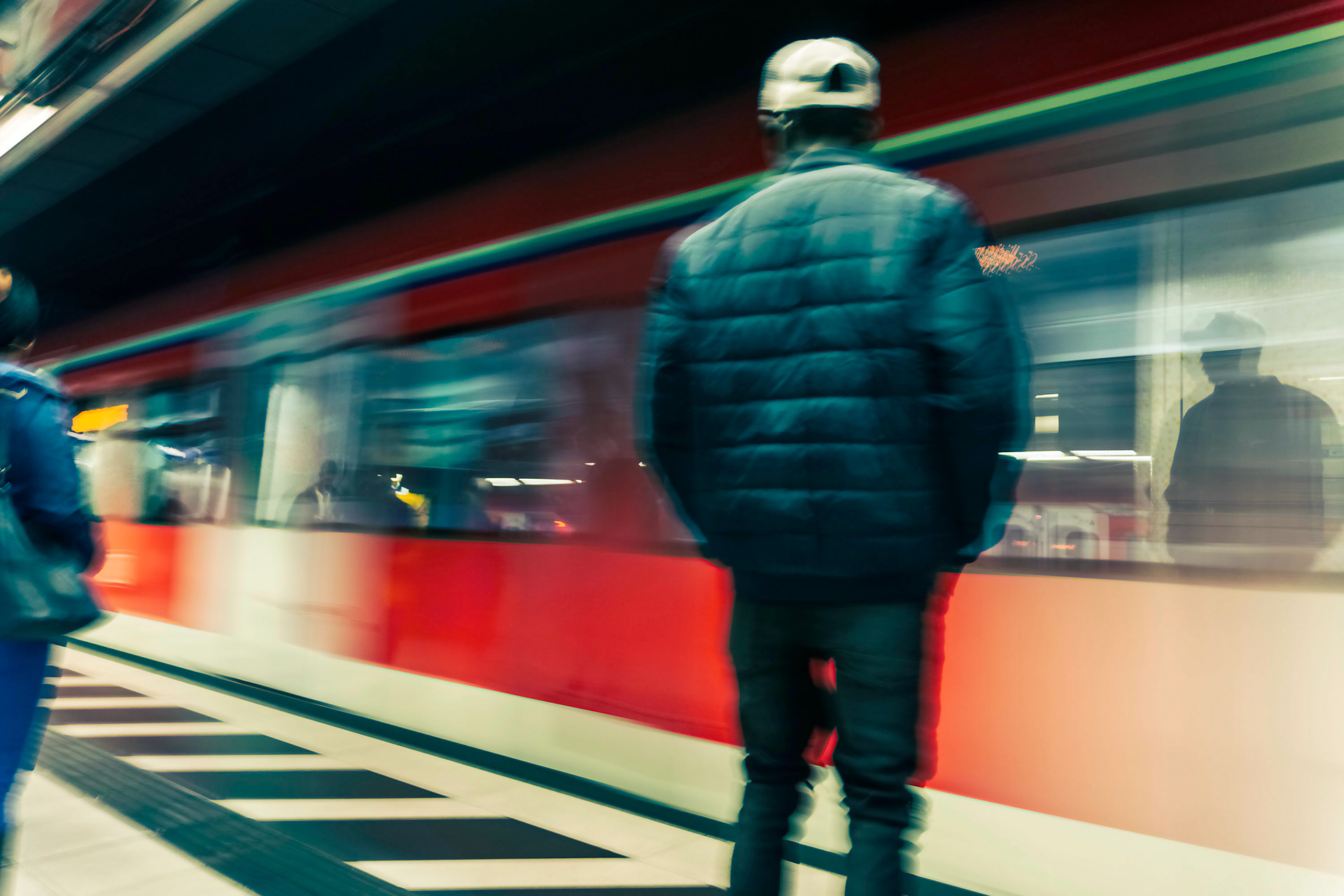 S-Bahn Station - Untergrund. Eine S-Bahn fährt ein. Reflexionen in den verwischten Fenstern. Der Mann mit Baseballkappe ist kaum zu erkennen. Woher kommt er, wohin fährt er? Was denkt er? Alltag in der Großstadt.