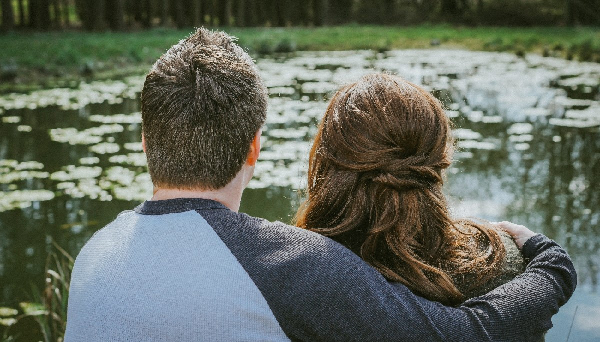 soon to be bride and groom sat holding each other looking out at lake next to endeavour woodland wedding venue in south england in buckinghamshire on a warm spring day with photographer david lefebvre