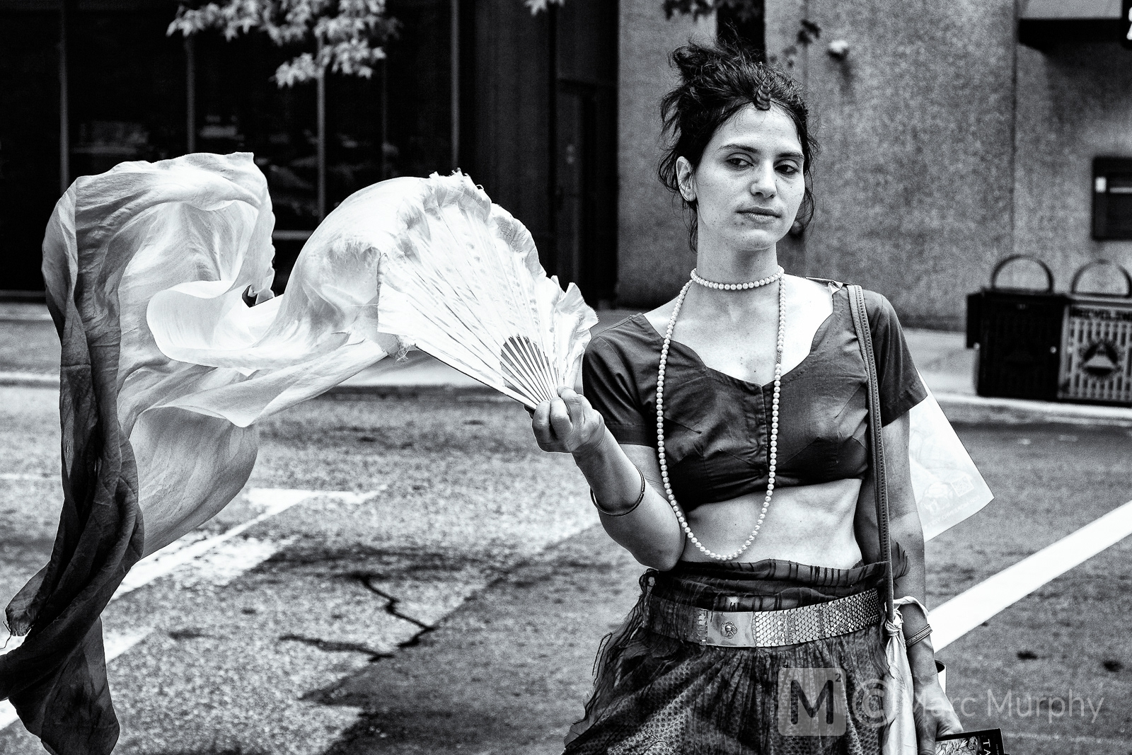 Black and White Gypsy Street Performer Wearing Long Pearl Necklace and Unicorn Horn and Waiving a Fan With Flowing Fabric Attached