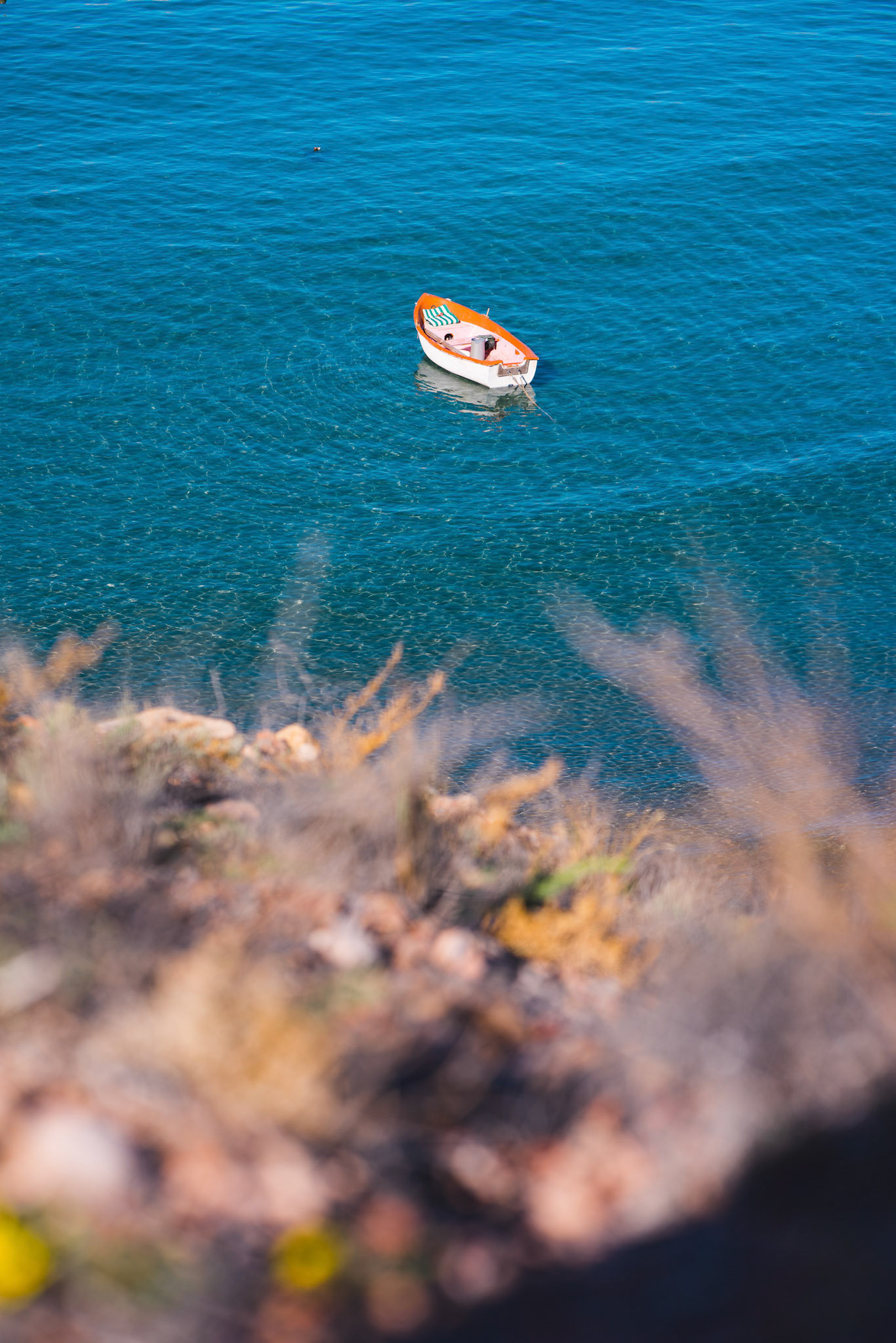 A lonesome boat moored in the bay. Deep blue see and a  small wooden boat.