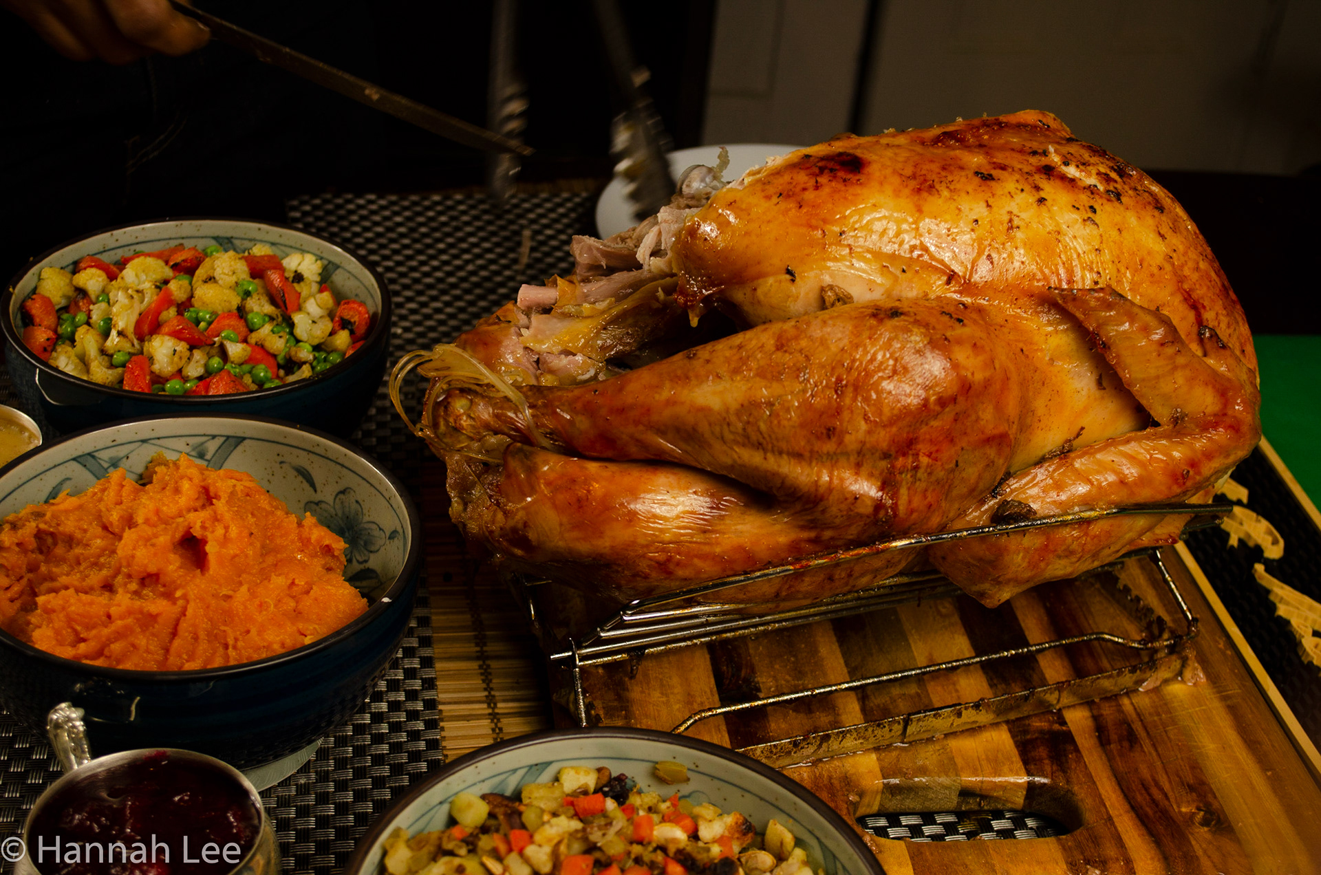 Damian cuts the turkey on Thanksgiving. Turkey stands next to cranberry sauce, stuffing, roasted butternut squash mash, and roasted vegetables: peas, carrots, and celery. Taken by Hannah Lee on November 26, 2020 in Somerville, MA. 1/60 second f 5.0 34 mm iso 250
