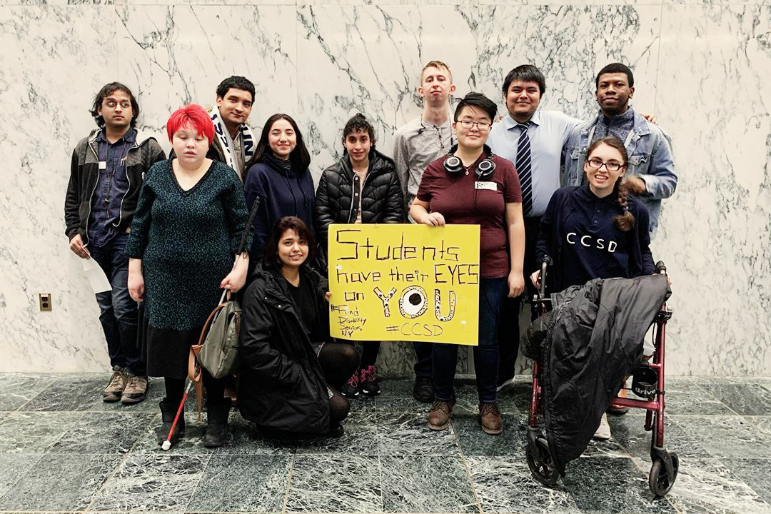 Group of students holding a sign saying "Students have their eyes on you," with an unnerving eye drawn into the "O" in "you"