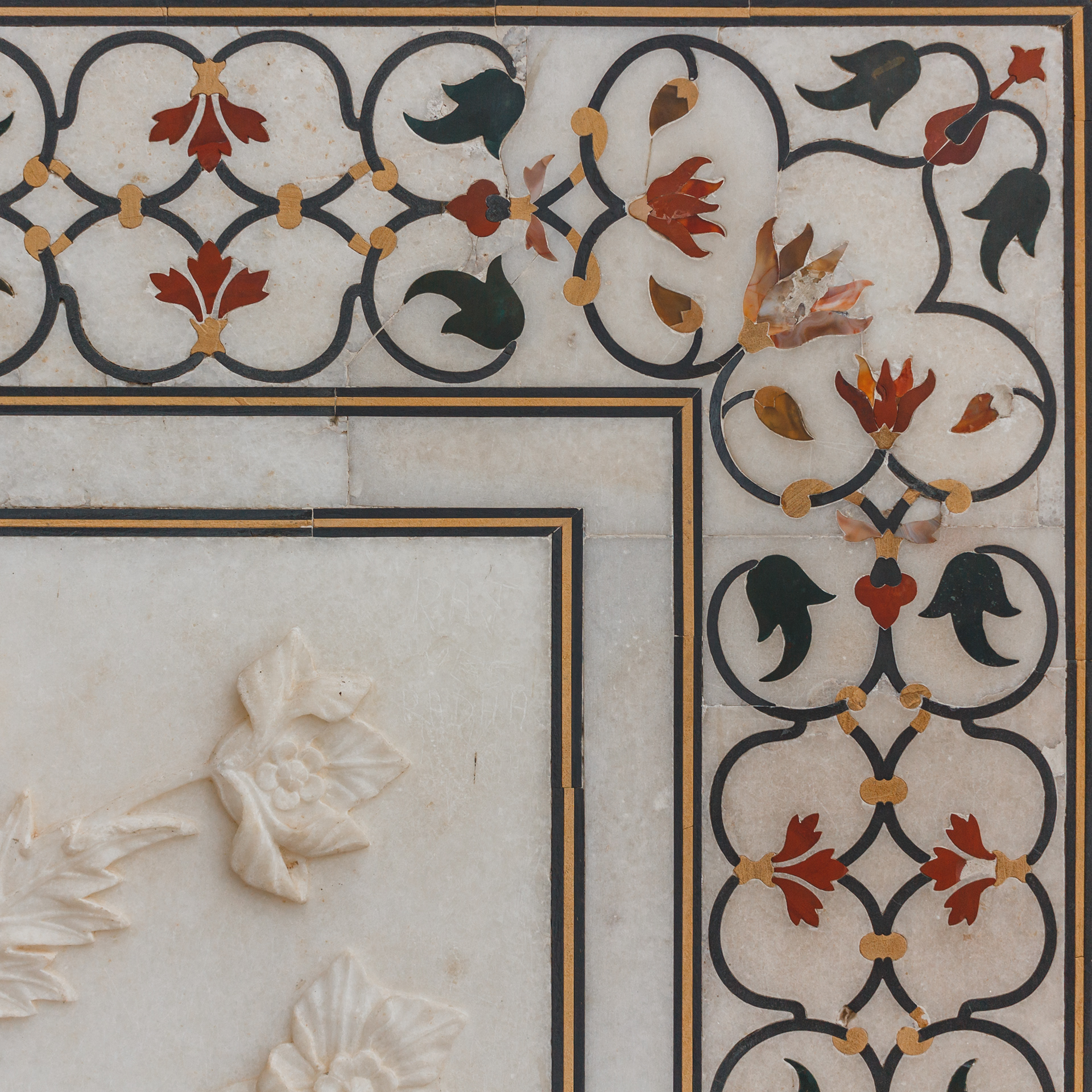 Up close detail of the Taj Mahal, showing the carefully carved marble flowers and the jewel/stone insets in dark green, gold, red stones