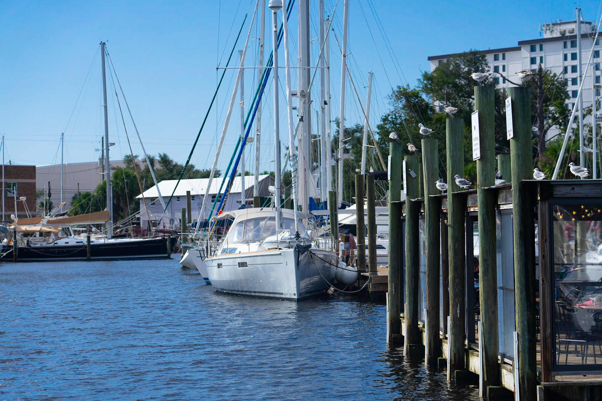 Leading Lines: Boat in the bayou, Using the boat's surroundings to draw you back to the boat, 20201029, Historic Panama City, MILLER, Setting up this shot, I positioned my self in way that the surrounding would draw you back to the boat. The roof and deck line of the restaurant create vanish points back to the boat, the black boat to the left leads you to the sail boat, and the masts and rigging on the boats also draw you down to the sail boat of focus. Camera Settings: Sony A7 II, ISO 200, 92mm, f4.5, 1/2500s