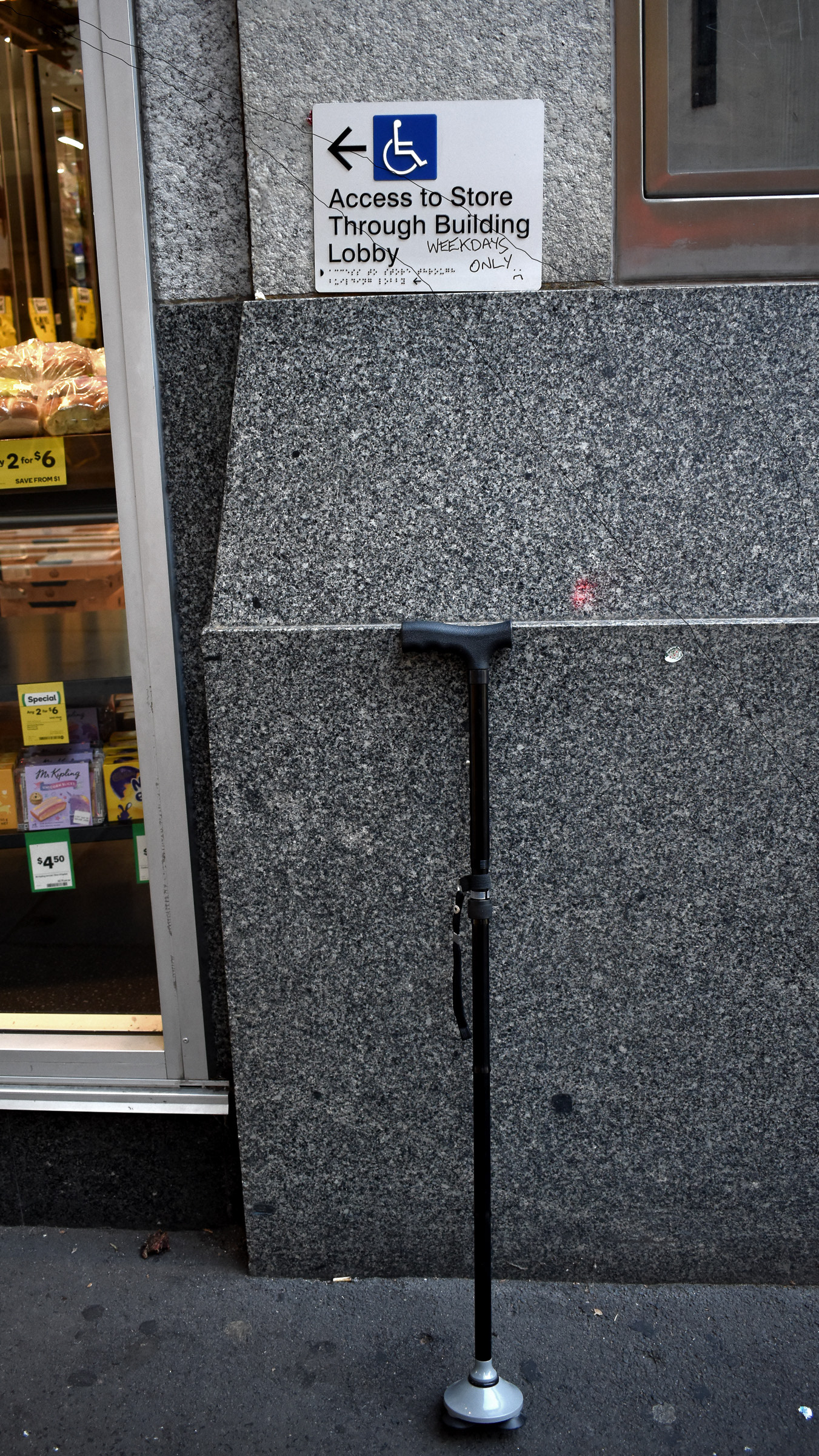 A cane, next to a grocery store and a wheelchair access sign that's on 'weekdays only'