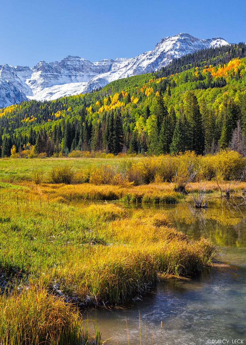Snow-capped peaks of the San Juan Mountains and pond in forest meadow in early Autumn, Colorado