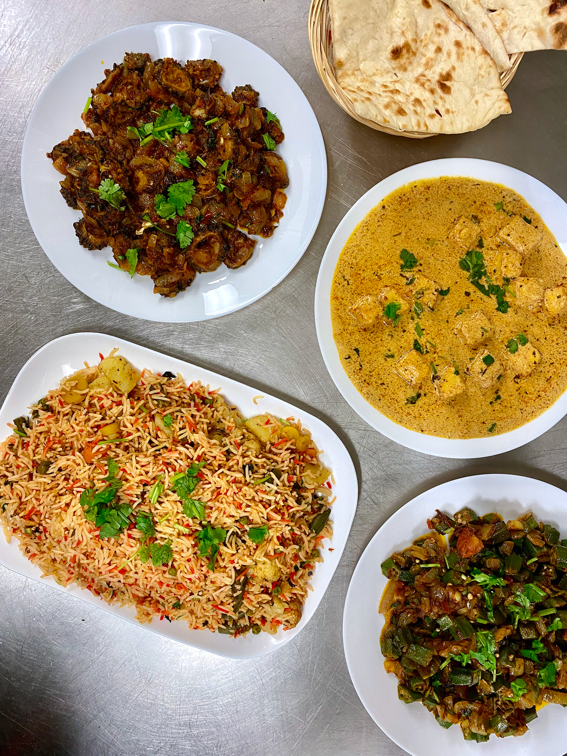 A variety of Indian and Pakistani foods including karela, shaahi paneer, vegetable biryani, bhindi and naan.
