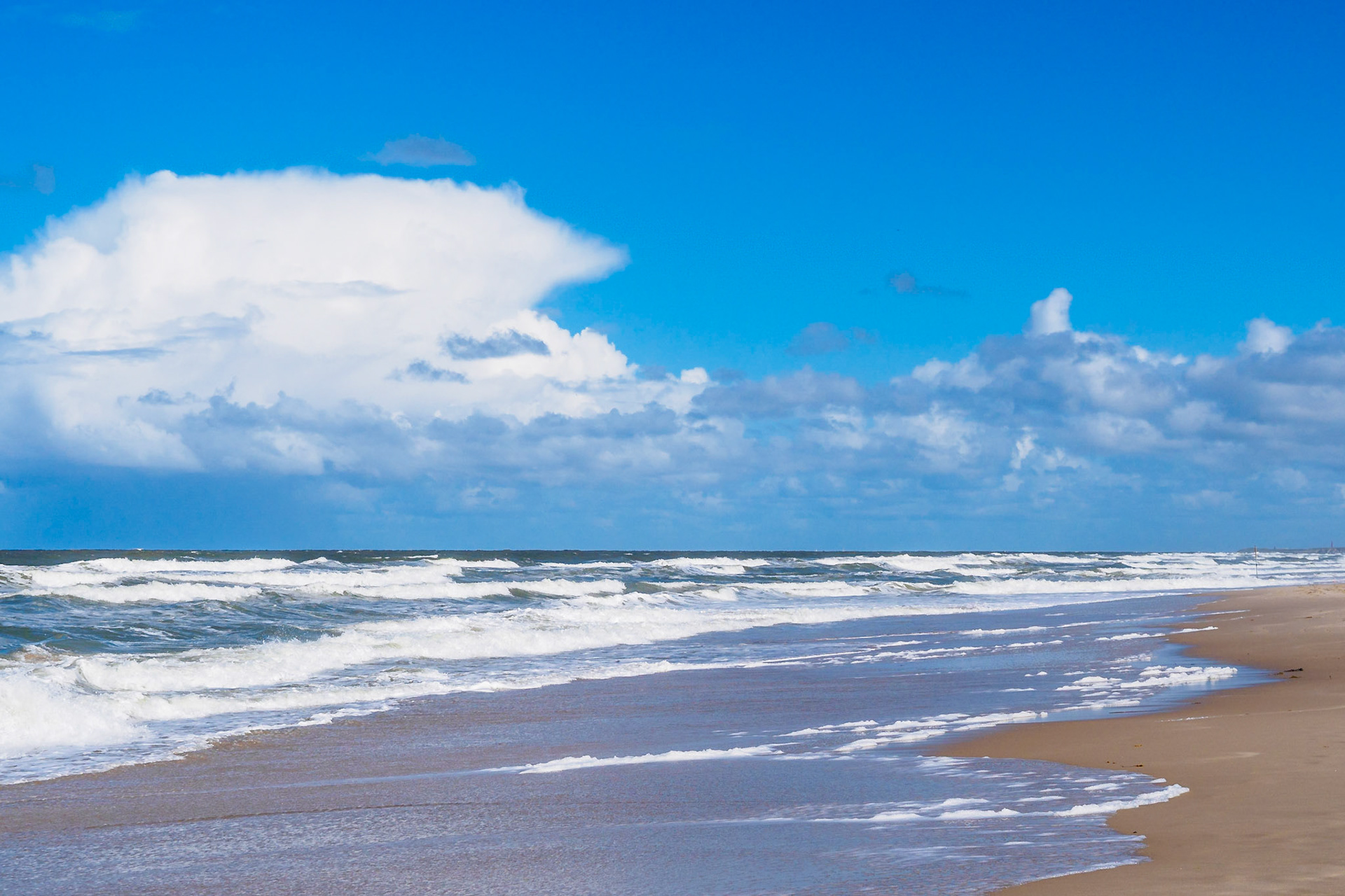 White foaming waves under a blue cloud-rich sky