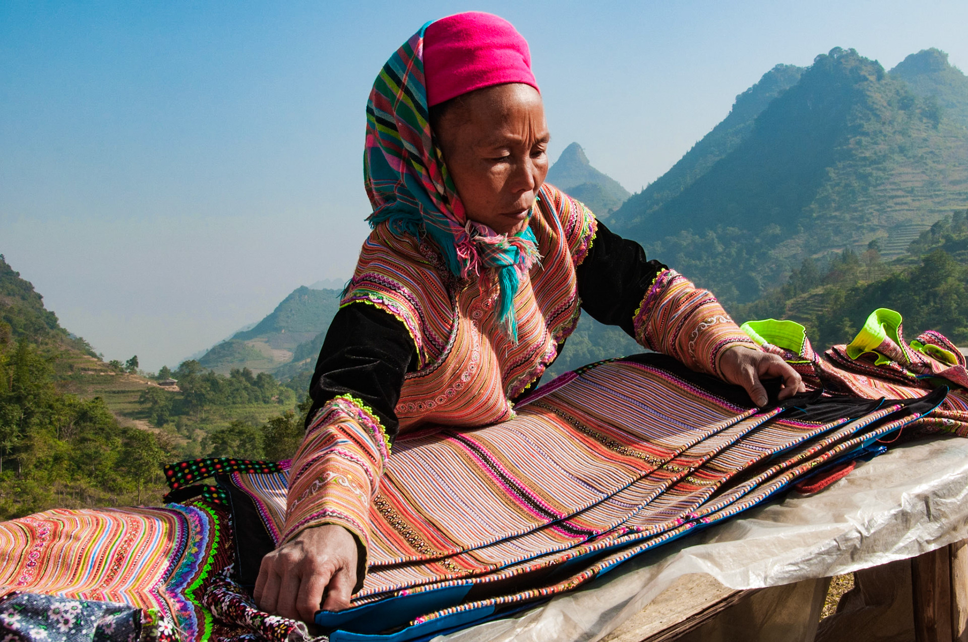 Vietnam, northern. Portrait of a flower Hmong hill tribe woman is spreading out some cloth that she hopes to sell. This is the Can Cao Market, and behind are limestone hills.