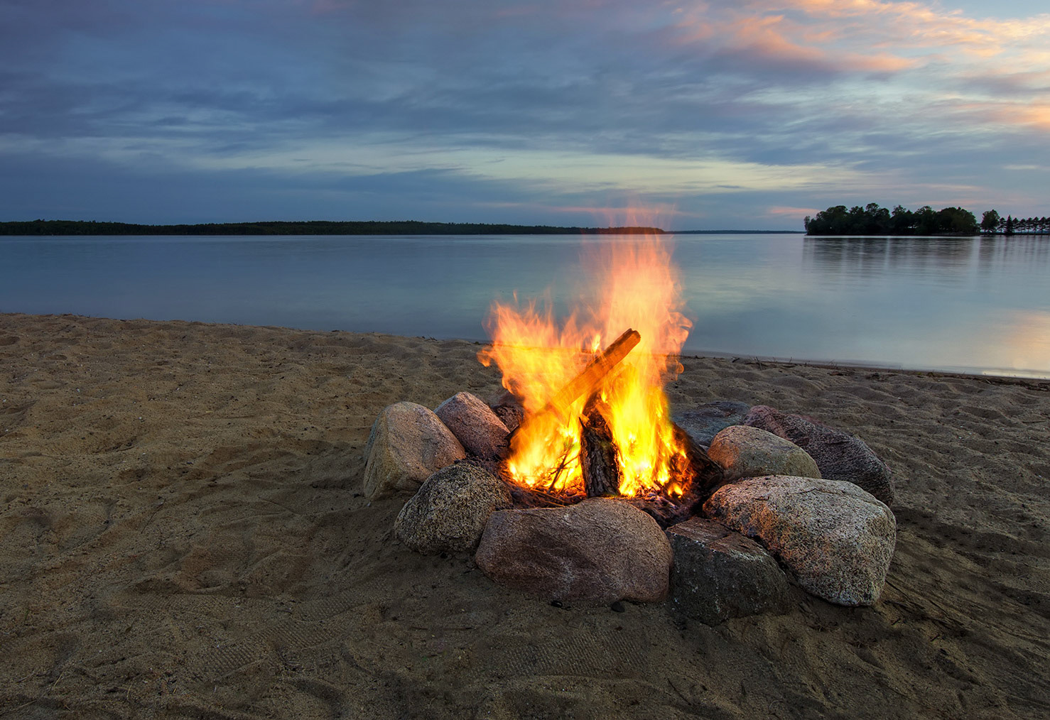 Camp fire on sandy beach, beside lake at sunset. Minnesota, USA