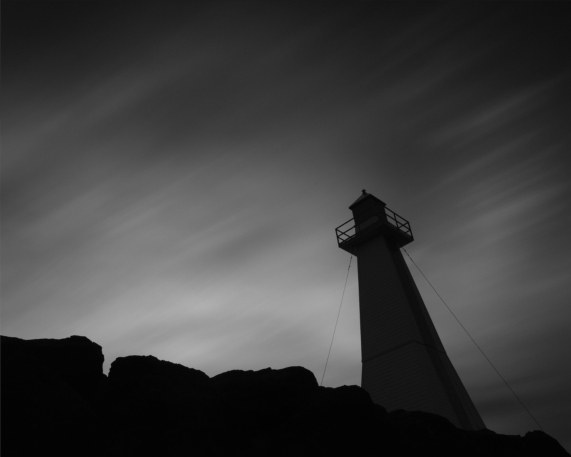 A long, black and white exposure of a lighthouse along a rocky coast